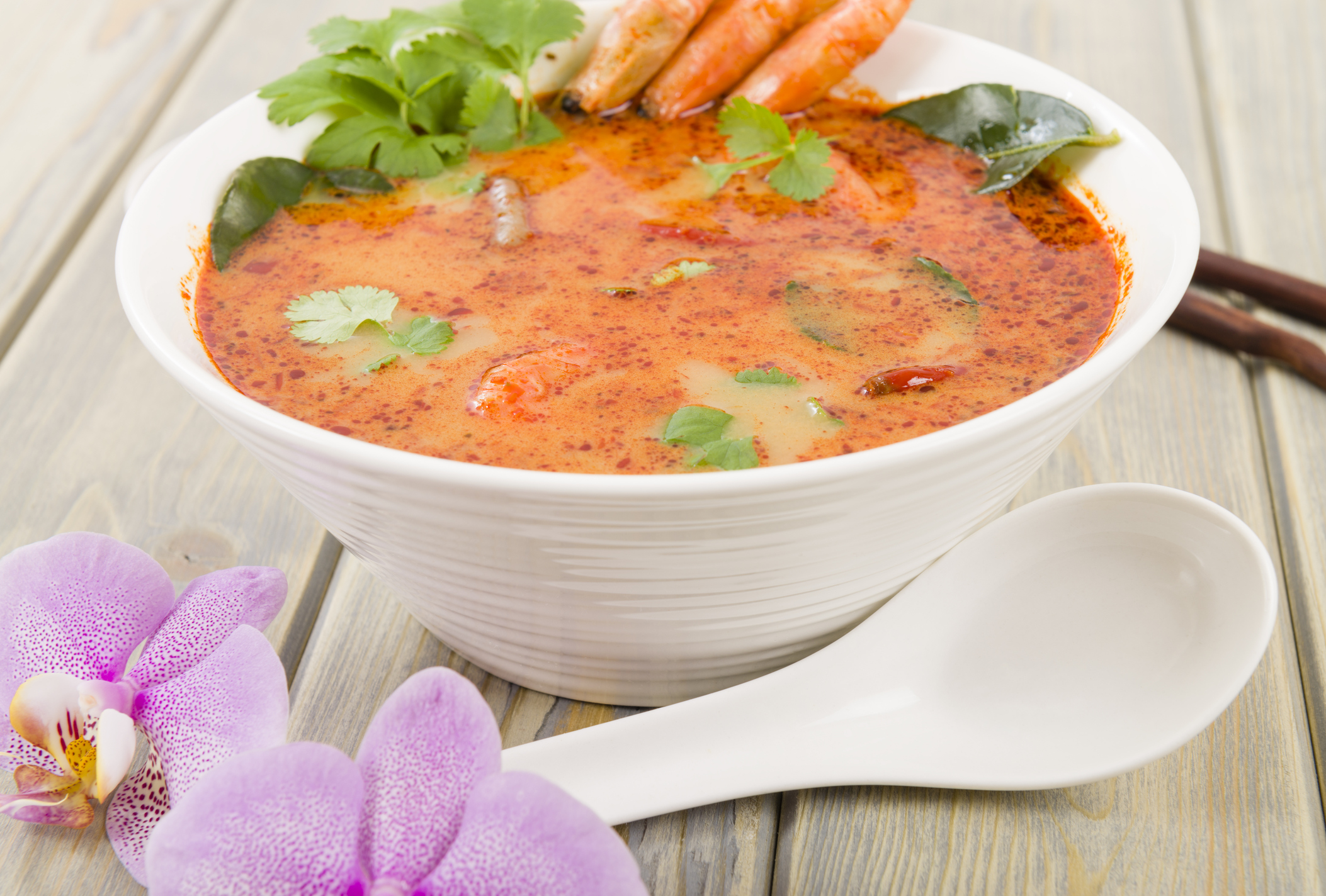 Creamy Thai soup with prawns and mushrooms garnished with coriander leaves and served with lime wedges.
